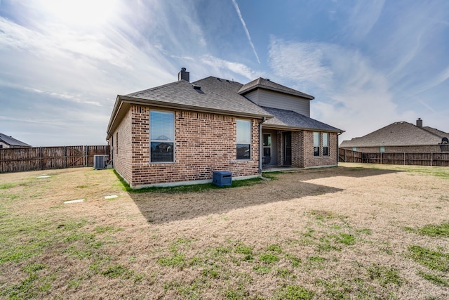 back of house featuring a shingled roof, a fenced backyard, brick siding, and central AC unit