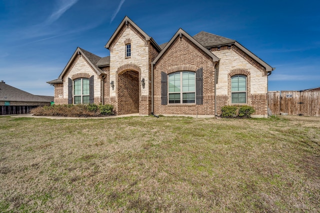 french country style house with a front yard, stone siding, brick siding, and roof with shingles