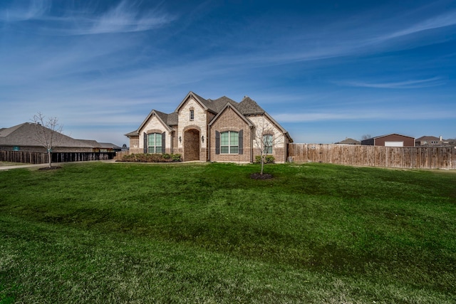 french country home with a front yard, brick siding, and fence