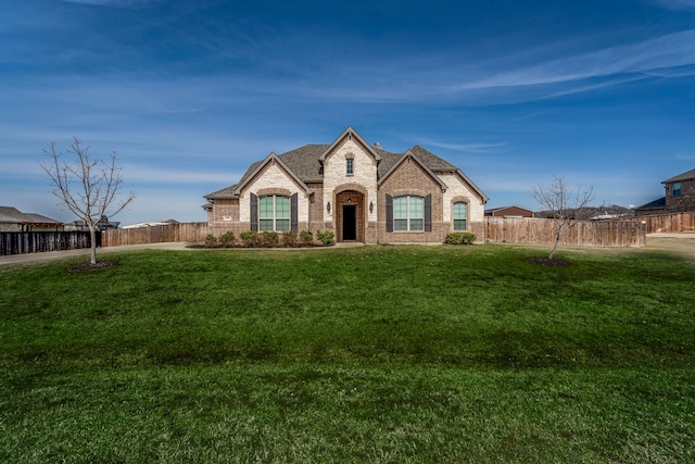 french country style house with brick siding, a front yard, and fence