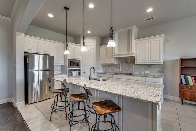 kitchen featuring a sink, visible vents, white cabinetry, appliances with stainless steel finishes, and a center island with sink