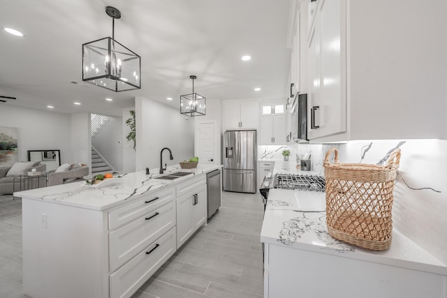 kitchen featuring a kitchen island with sink, stainless steel appliances, a sink, white cabinets, and decorative light fixtures