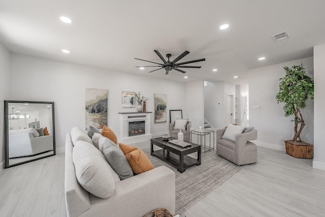 living area with light wood-style flooring, a glass covered fireplace, visible vents, and recessed lighting