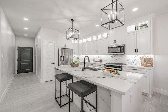 kitchen with stainless steel appliances, glass insert cabinets, a kitchen island with sink, a sink, and white cabinetry