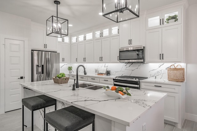 kitchen featuring stainless steel appliances, glass insert cabinets, a center island with sink, and a sink