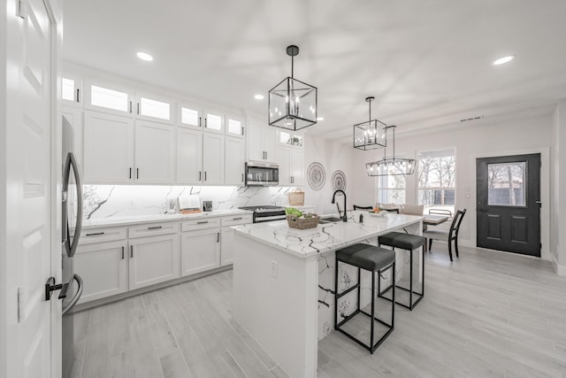 kitchen with stainless steel appliances, a kitchen island with sink, and white cabinetry