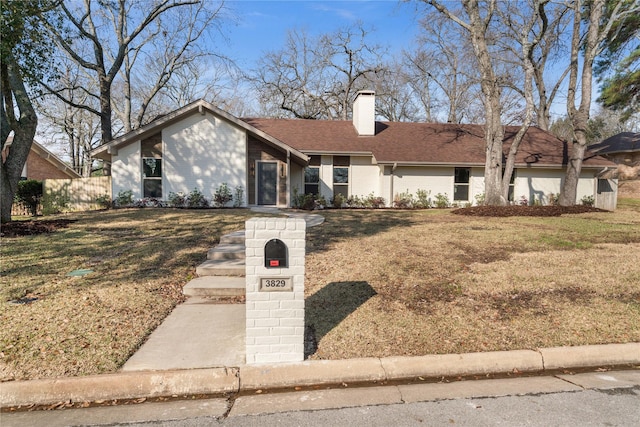 mid-century inspired home featuring a shingled roof, a chimney, fence, a front lawn, and brick siding