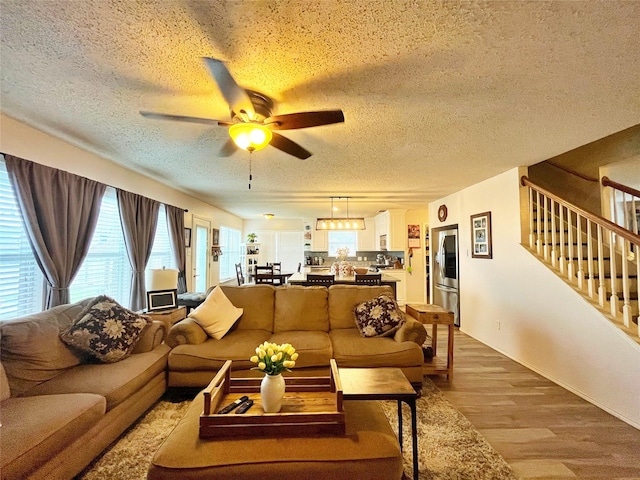 living room with stairs, ceiling fan, a textured ceiling, and light wood-type flooring