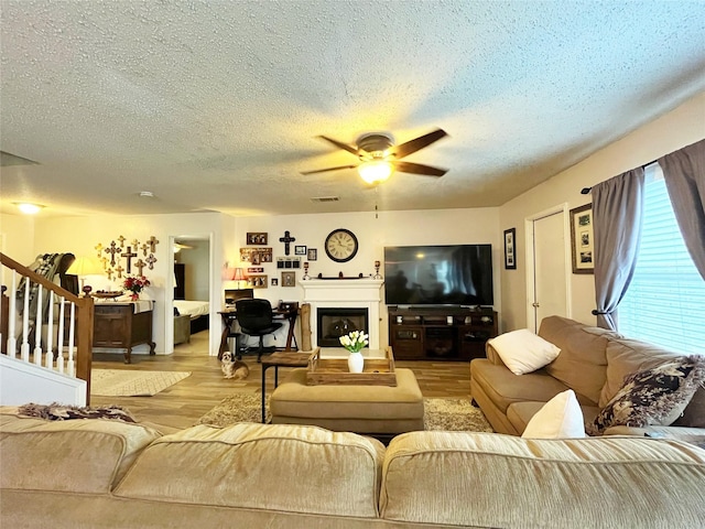 living area with visible vents, light wood-style flooring, a glass covered fireplace, ceiling fan, and stairs