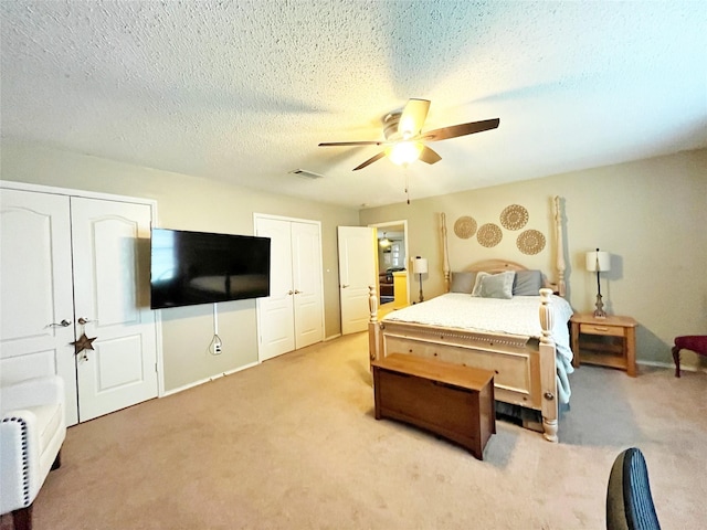 bedroom with multiple closets, light colored carpet, visible vents, a ceiling fan, and a textured ceiling