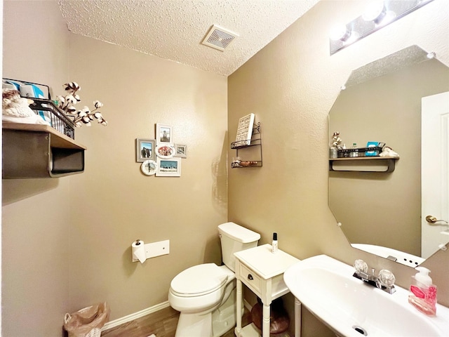 half bath with visible vents, toilet, a sink, a textured ceiling, and wood finished floors