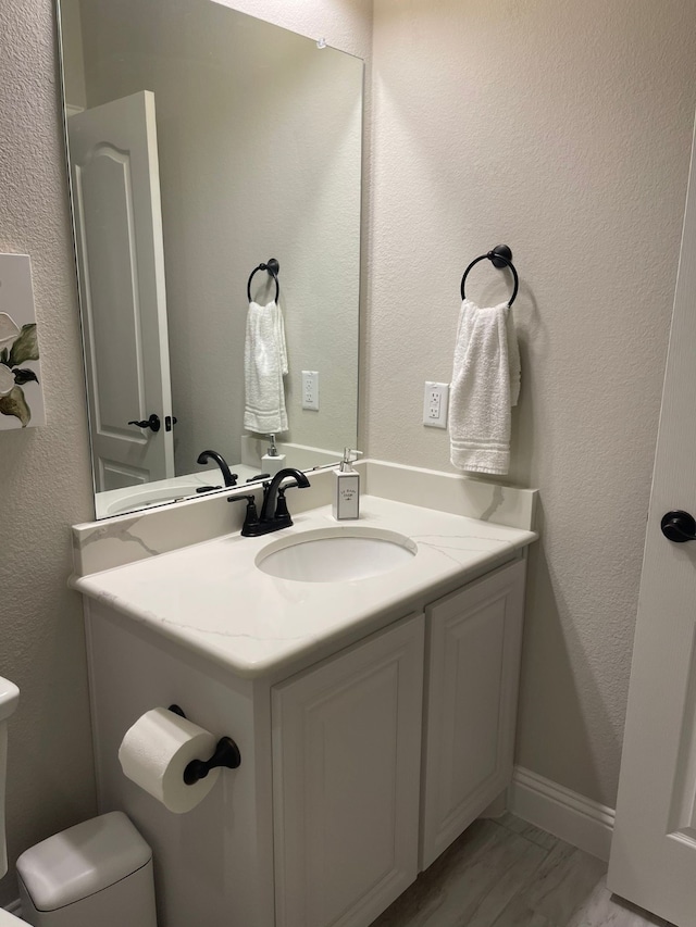 bathroom featuring toilet, a textured wall, baseboards, and vanity