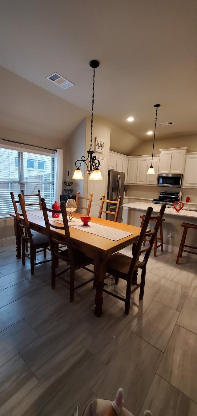 dining space featuring visible vents, vaulted ceiling, and wood finished floors