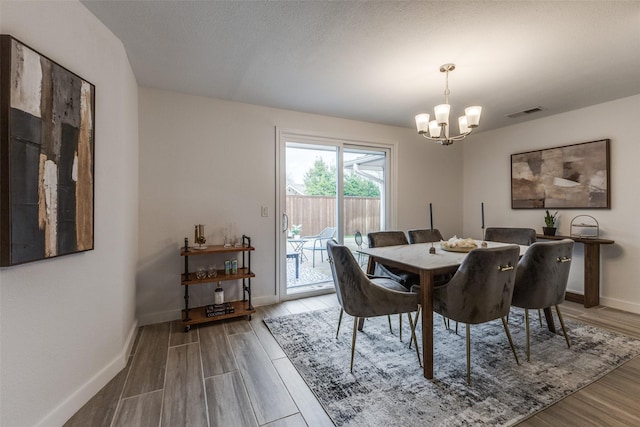 dining space featuring a chandelier, wood finished floors, visible vents, and baseboards