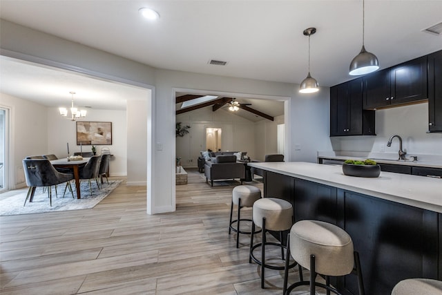 kitchen with open floor plan, a kitchen breakfast bar, light countertops, dark cabinetry, and pendant lighting