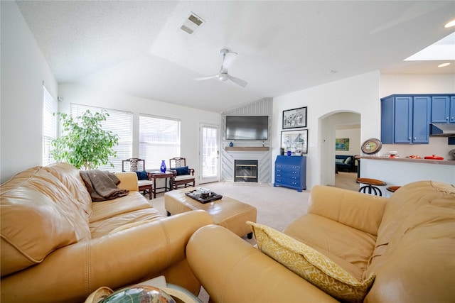 living room with light carpet, a large fireplace, arched walkways, ceiling fan, and vaulted ceiling