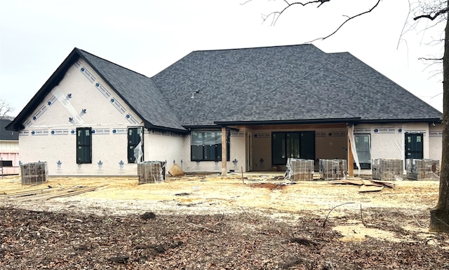 rear view of house featuring a shingled roof and stucco siding