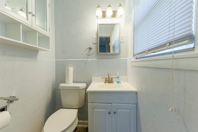 bathroom featuring toilet, a textured wall, tile walls, and vanity