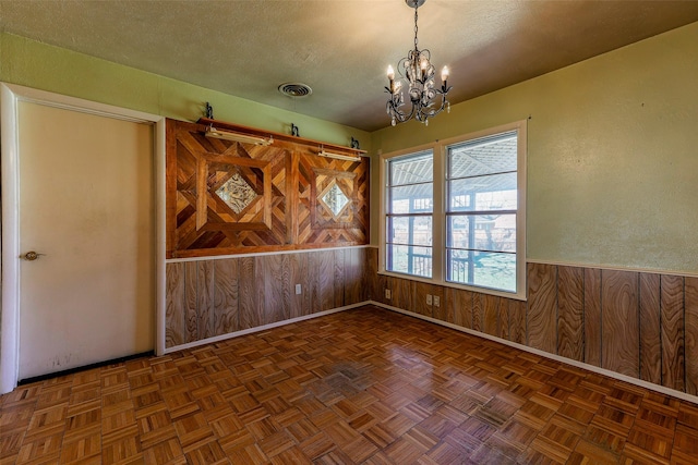 unfurnished room with a textured ceiling, a notable chandelier, a wainscoted wall, wood walls, and visible vents