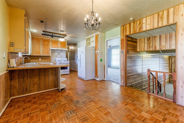 kitchen with a peninsula, white appliances, wood walls, a sink, and light countertops