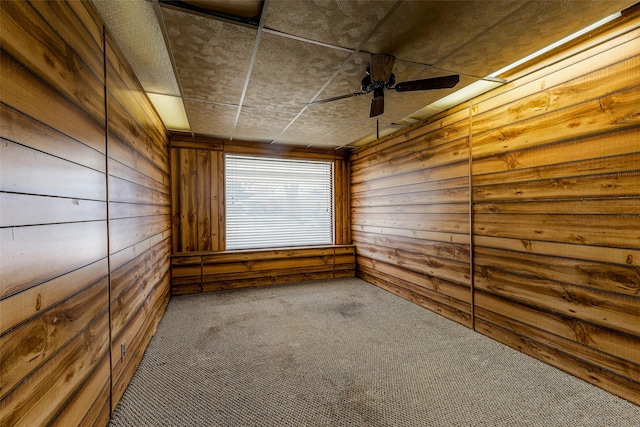 carpeted empty room featuring a ceiling fan and wooden walls