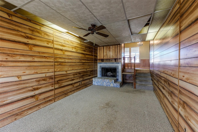 unfurnished living room with carpet floors, wooden walls, a fireplace with raised hearth, and a ceiling fan