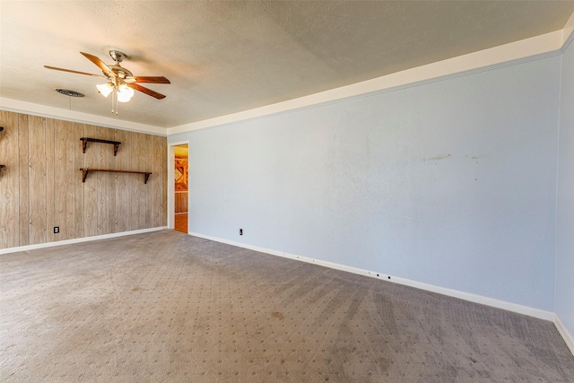 carpeted empty room featuring ceiling fan, a textured ceiling, wooden walls, visible vents, and baseboards