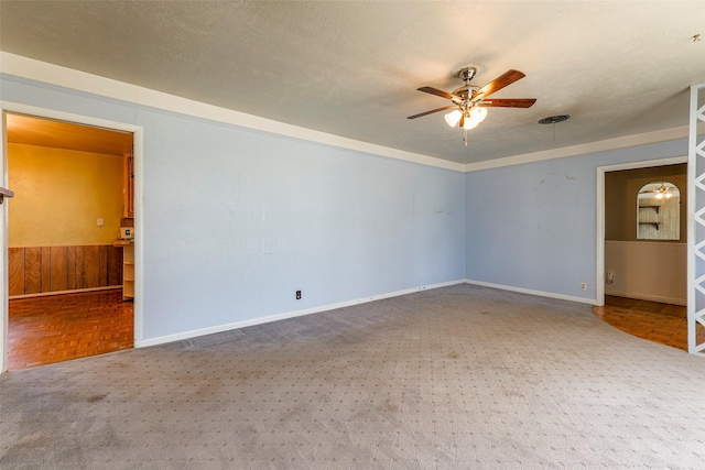 carpeted spare room with a textured ceiling, visible vents, a ceiling fan, and a wainscoted wall