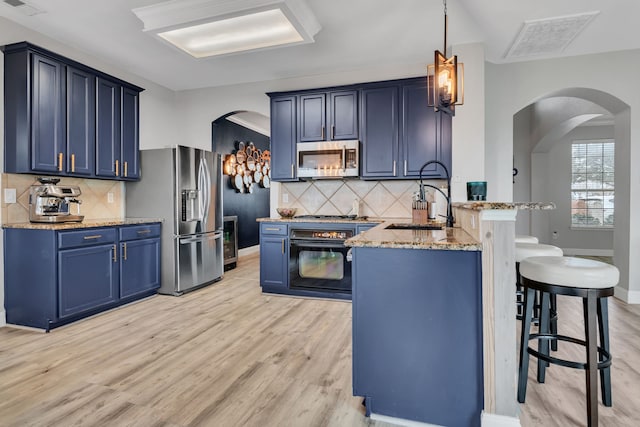 kitchen with decorative light fixtures, appliances with stainless steel finishes, a sink, blue cabinets, and a peninsula