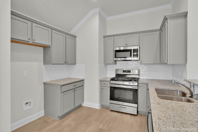 kitchen with light wood finished floors, appliances with stainless steel finishes, a sink, and ornamental molding