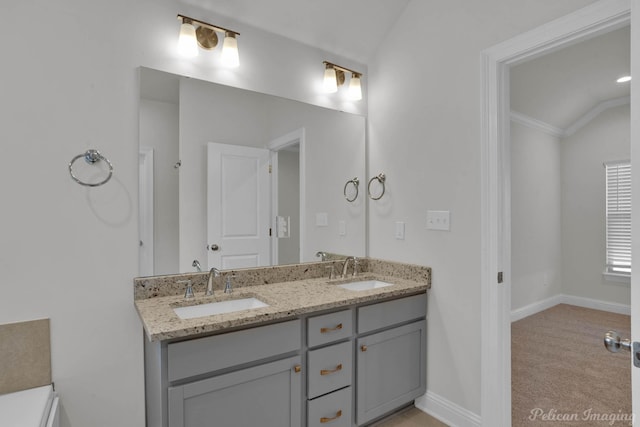 bathroom with vaulted ceiling, double vanity, a sink, and baseboards