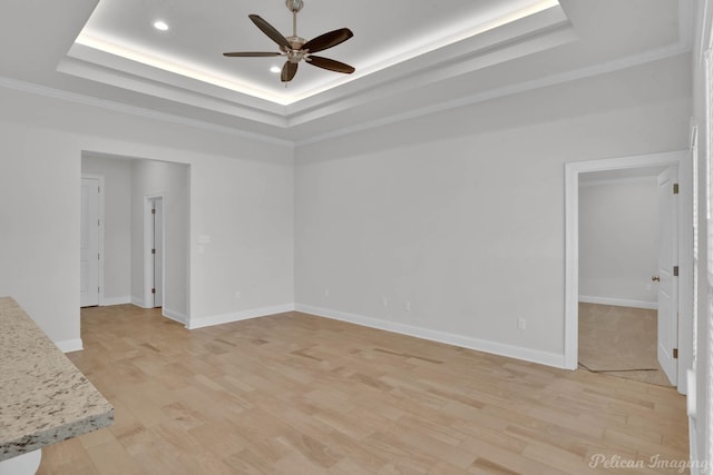 empty room with light wood-style floors, a tray ceiling, baseboards, and a ceiling fan