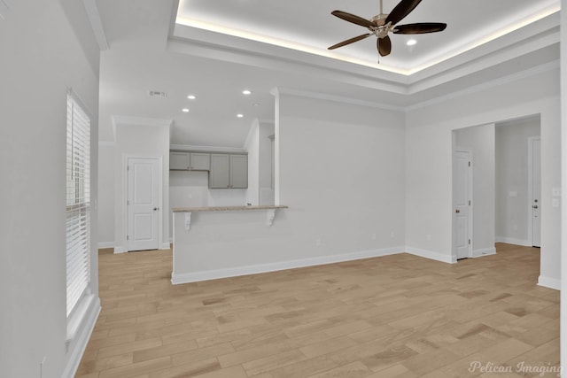 unfurnished living room featuring baseboards, a raised ceiling, ceiling fan, ornamental molding, and light wood-type flooring