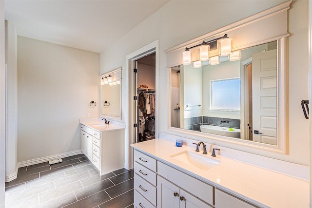 bathroom with a spacious closet, baseboards, two vanities, and a sink