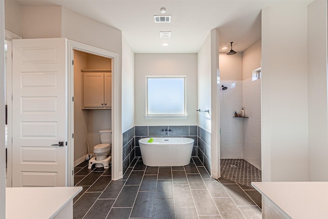 bathroom featuring visible vents, toilet, walk in shower, a freestanding bath, and tile walls