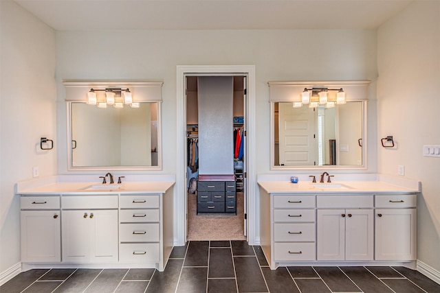 bathroom with a walk in closet, two vanities, a sink, and baseboards