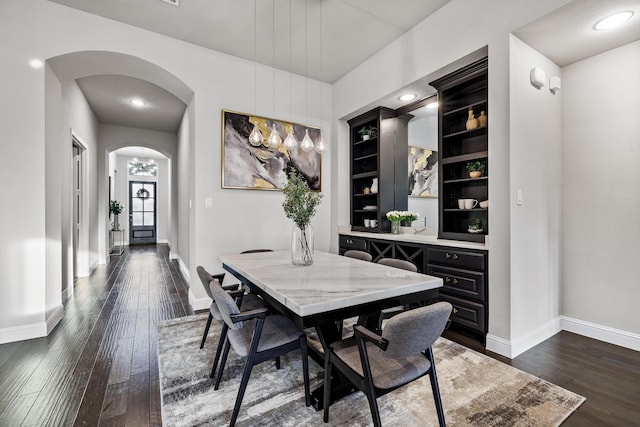 dining space with dark wood-style floors, arched walkways, and baseboards