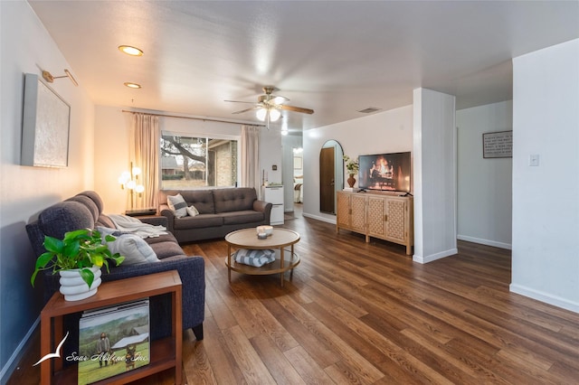 living room featuring baseboards, arched walkways, visible vents, ceiling fan, and wood finished floors