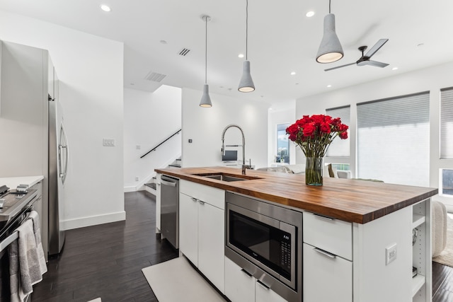 kitchen featuring white cabinets, appliances with stainless steel finishes, wooden counters, and decorative light fixtures