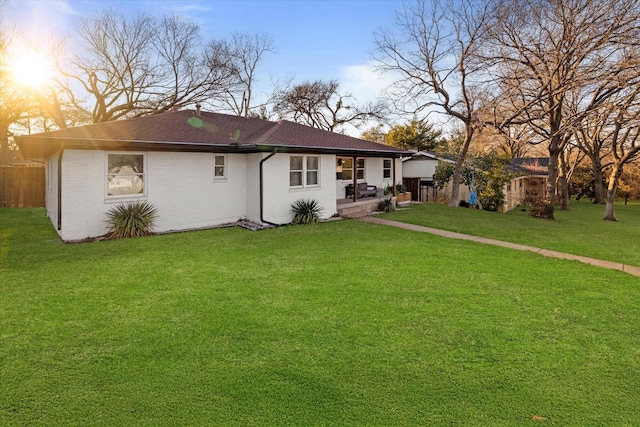 back of house at dusk featuring roof with shingles, brick siding, and a lawn