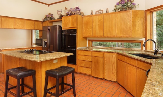 kitchen featuring brick floor, a breakfast bar, a sink, a center island, and black appliances