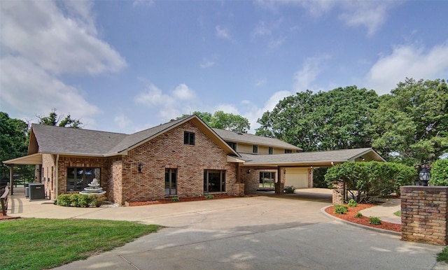 view of front of property with an attached garage, central AC, brick siding, a shingled roof, and driveway