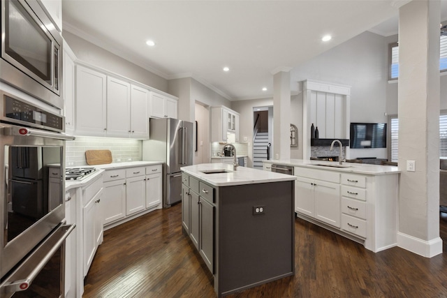 kitchen featuring a peninsula, a center island with sink, white cabinetry, and stainless steel appliances