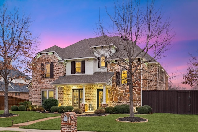 view of front of house featuring a shingled roof, a front yard, brick siding, and fence