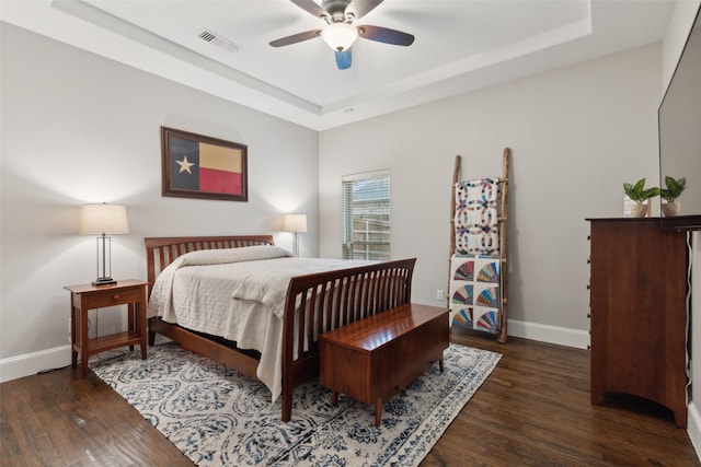 bedroom featuring baseboards, visible vents, a tray ceiling, and dark wood-style flooring