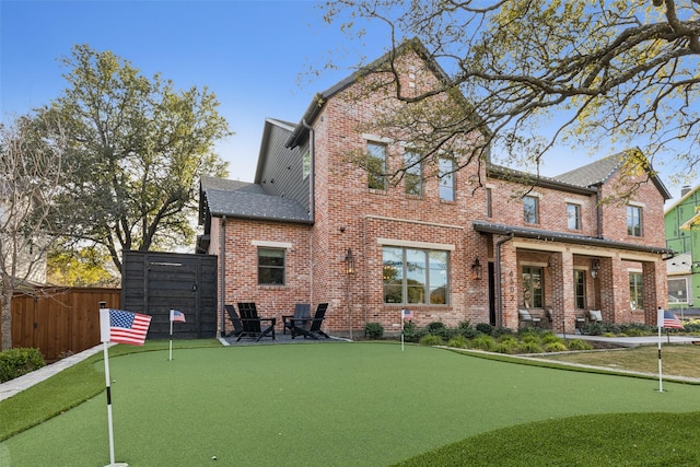 back of property featuring brick siding, a shingled roof, and fence