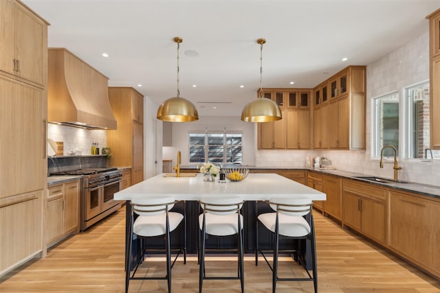 kitchen with a sink, wall chimney range hood, an island with sink, double oven range, and a kitchen breakfast bar