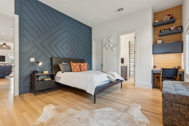 bedroom with visible vents, an accent wall, ensuite bath, light wood-type flooring, and baseboards