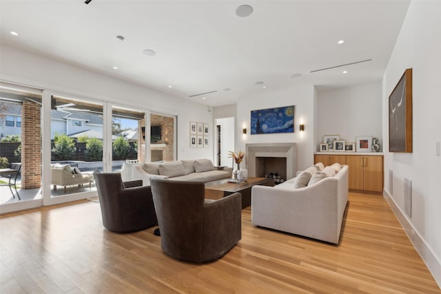 living area with baseboards, light wood-type flooring, a fireplace, and recessed lighting