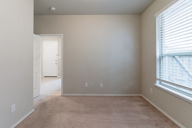 spare room with baseboards, a wealth of natural light, and light colored carpet